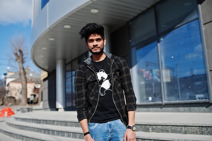 Foto gratuito hombre asiático con barba en ropa informal posando contra un nuevo edificio moderno