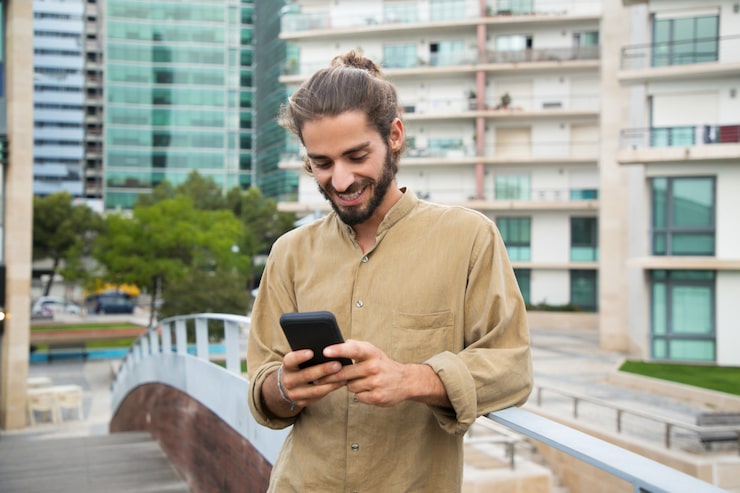 Foto gratuito un joven alegre usando un teléfono inteligente