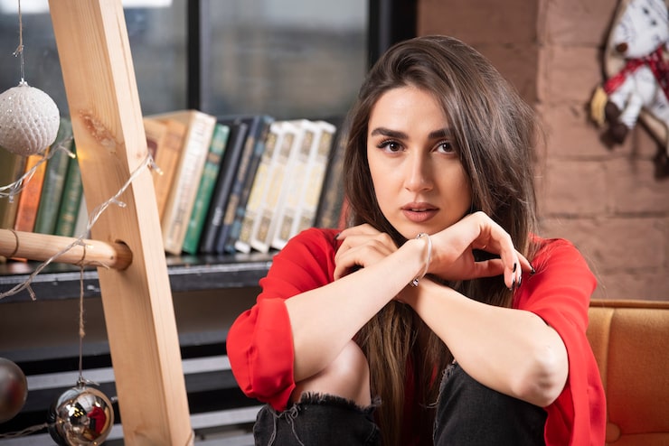 Foto gratuito un modelo de mujer joven en blusa roja sentada y posando.