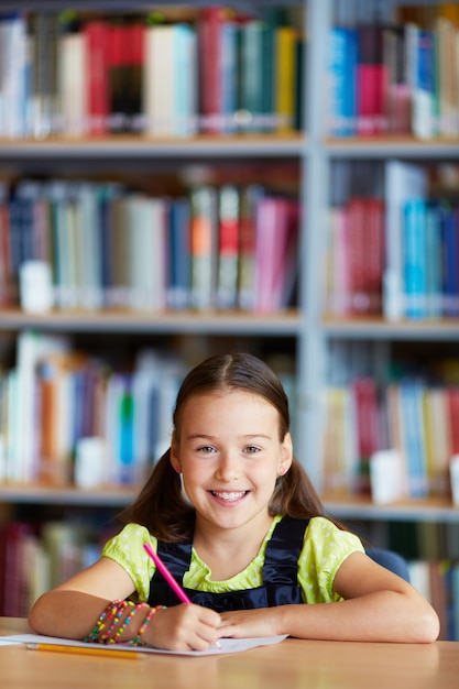 Foto gratuito niña sonriente dibujando en la biblioteca