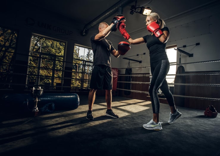 Foto gratuito en el oscuro gimnasio en el ring, la entrenadora experimentada y la joven tienen una pelea de kick boxing.