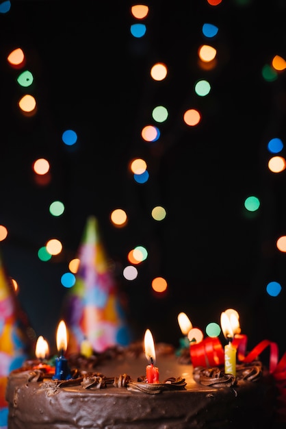 Foto gratuito pastel de chocolate con velas iluminadas y decorado con luces borrosas.