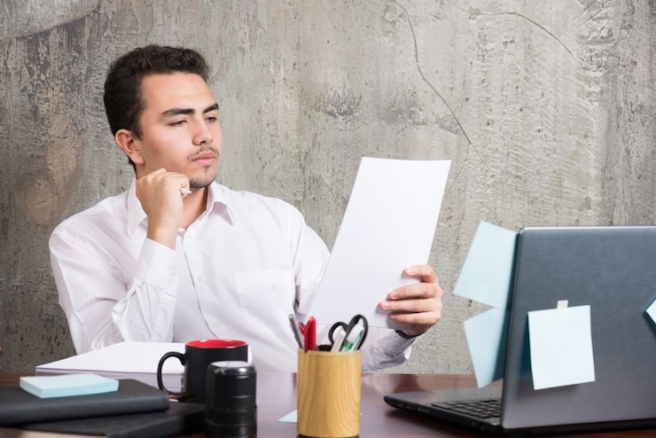 Photo Gratis pengusaha dengan hati-hati membaca kertas kerja di meja kantor.