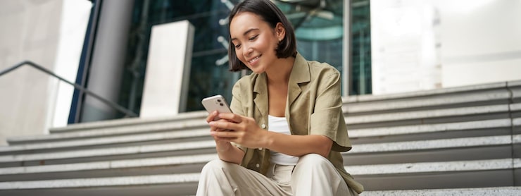 Foto gratuito tecnología y comunicación joven sonriente mujer asiática sentada con un teléfono inteligente lee el mensaje con