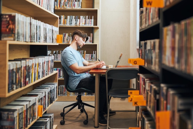Studente che impara in biblioteca giovane che si prepara a un test sul portatile uomo che ascolta un corso online