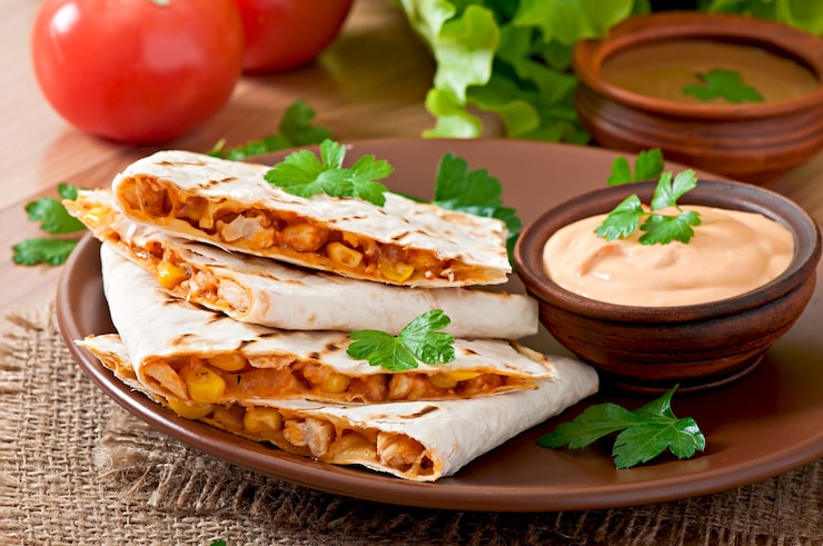 Zdarma Fotografie mexická quesadilla nakrájená s zeleninou a omáčkami na stole