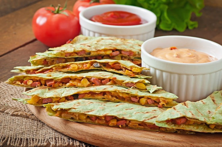 Zdarma Fotografie mexická quesadilla nakrájená s zeleninou a omáčkami na stole