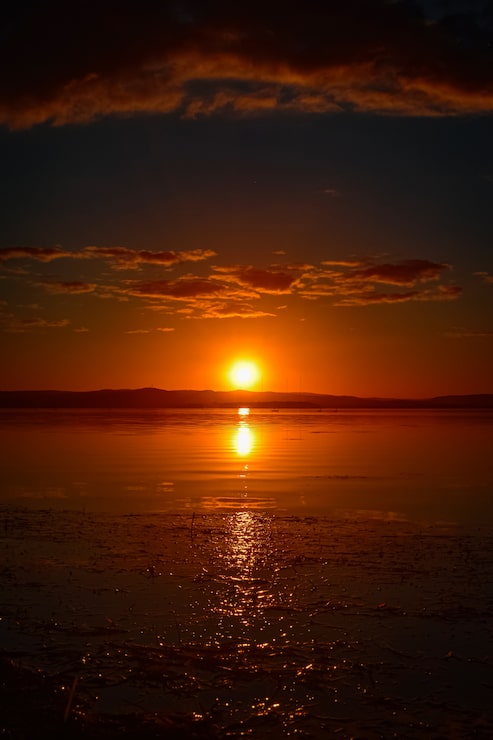 Foto grátis bela foto vertical do pôr-do-sol vermelho com nuvens no céu com reflexo na água