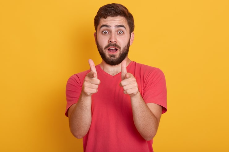 Foto grátis imagem de jovem bonito isolado sobre amarelo, olhando para a câmera e apontando com os dedos da frente