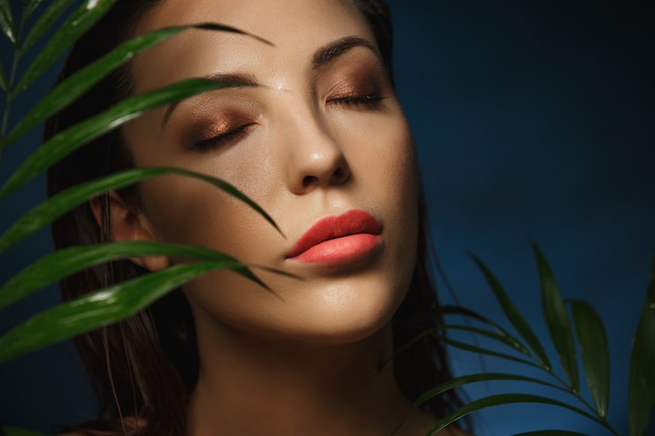 Gratis Bild vackert kvinnligt ansikte under exotiska gröna blad. modefotografering.