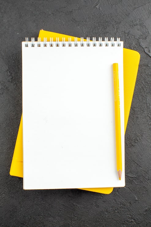 Photo gratuit crayon jaune de bloc-notes en spirale de vue de dessus sur le noir
